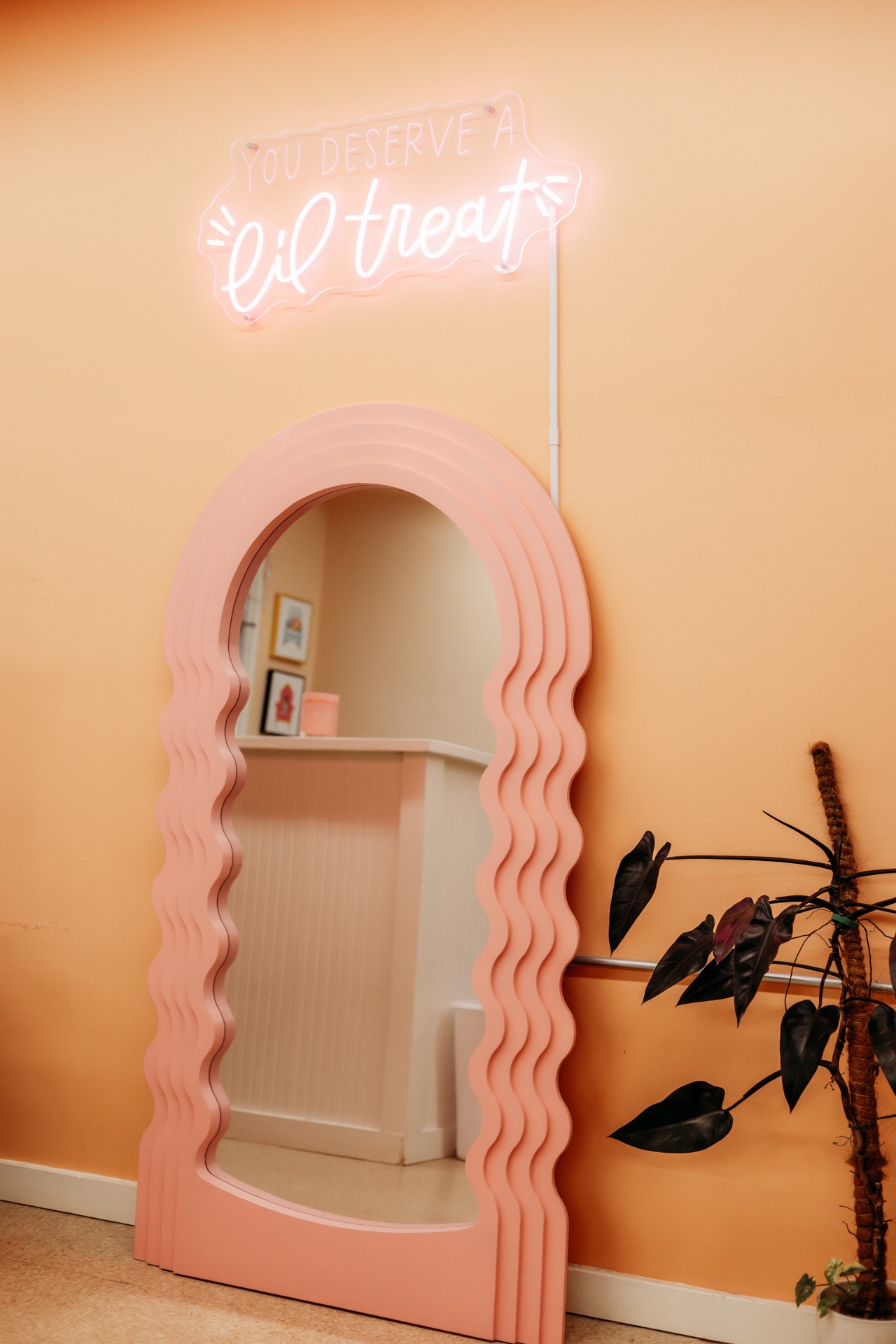 A pink wavy mirror and neon 'You deserve a lil treat' sign in the salon